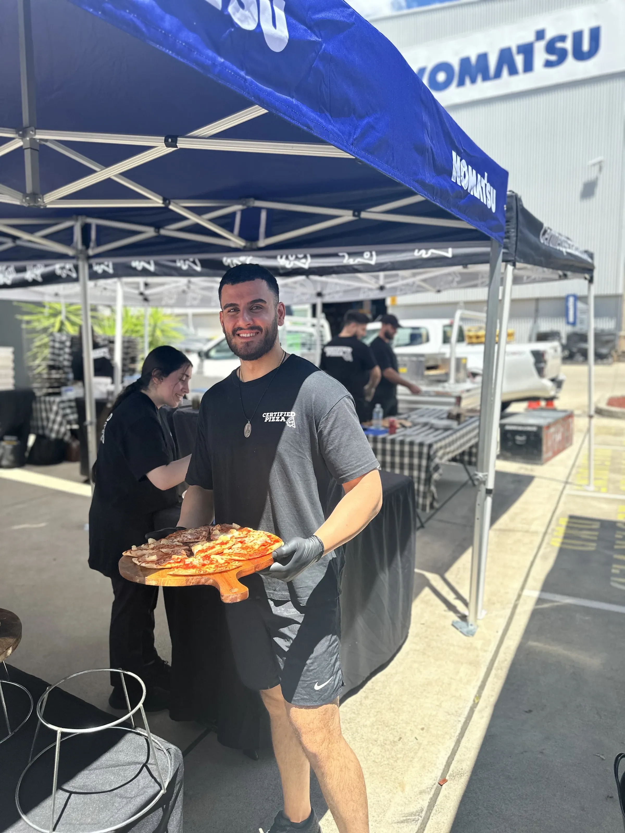 Certified Pizza team member holding fresh pizza slices at Komatsu Fairfield